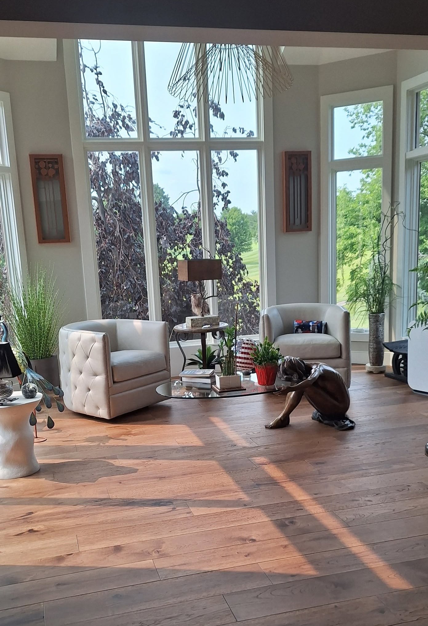 A sunlit living room with tall windows, tufted armchairs, and warm hardwood floors